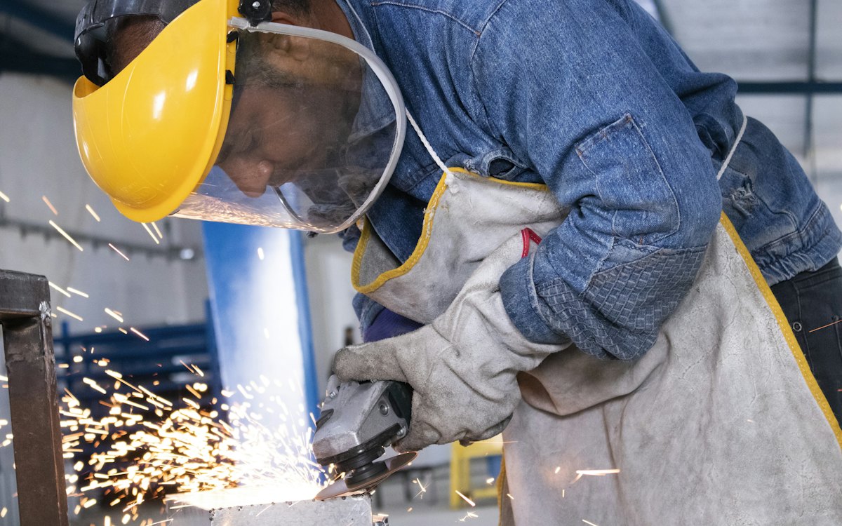 Trabalhador de máscara e capacete usando esmerilhadeira com faíscas