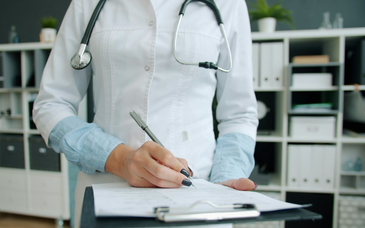 Médica preenchendo um documento em uma prancheta