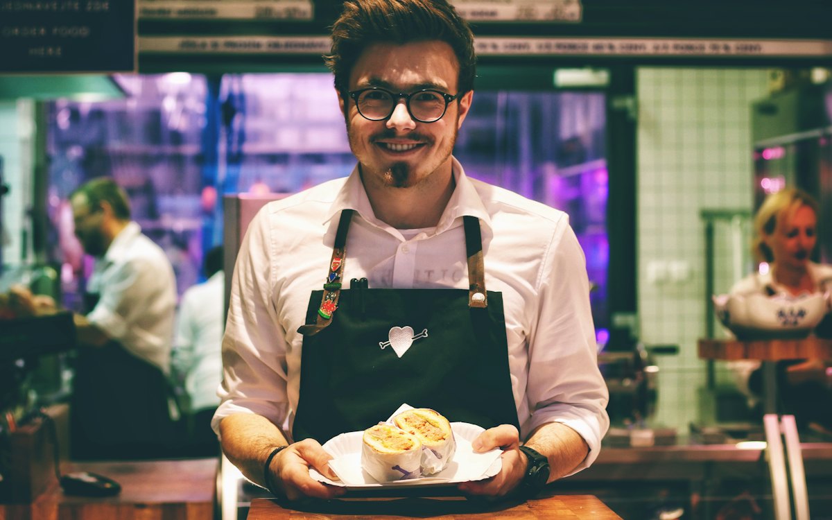 Garçom de avental segurando um prato no salão de um restaurante