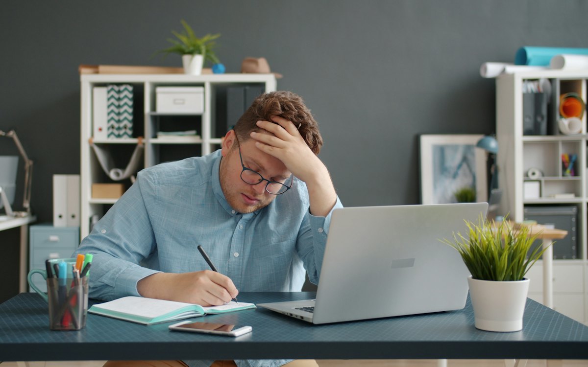 Homem preocupado com a mão na testa diante do notebook