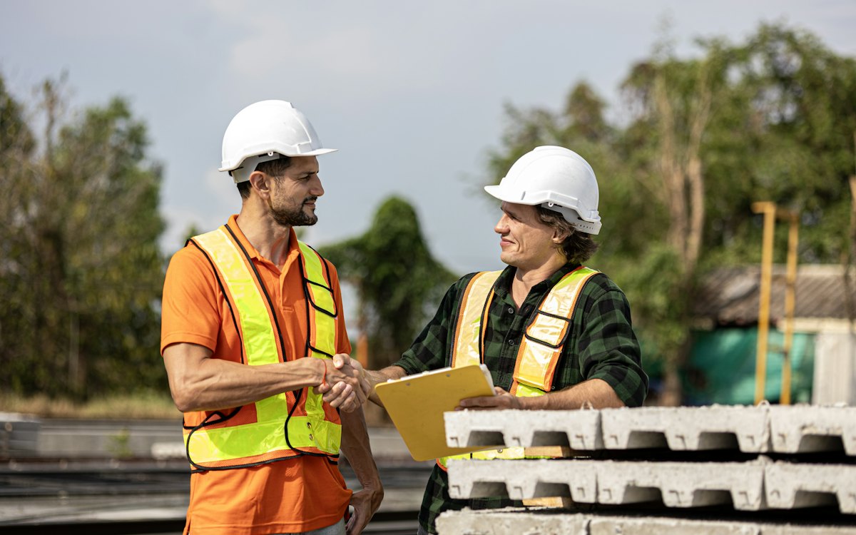 Dois trabalhadores com capacete e colete conversando em uma obra