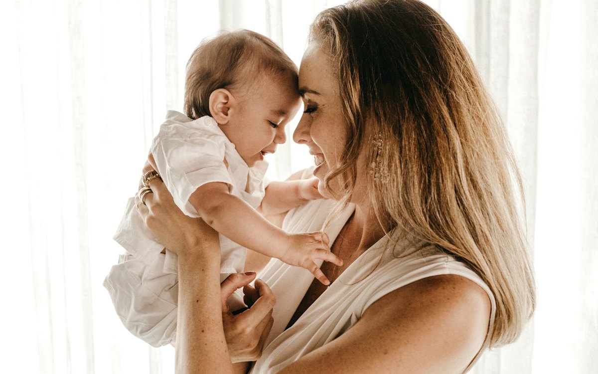 Mãe segurando o bebê no colo junto à janela
