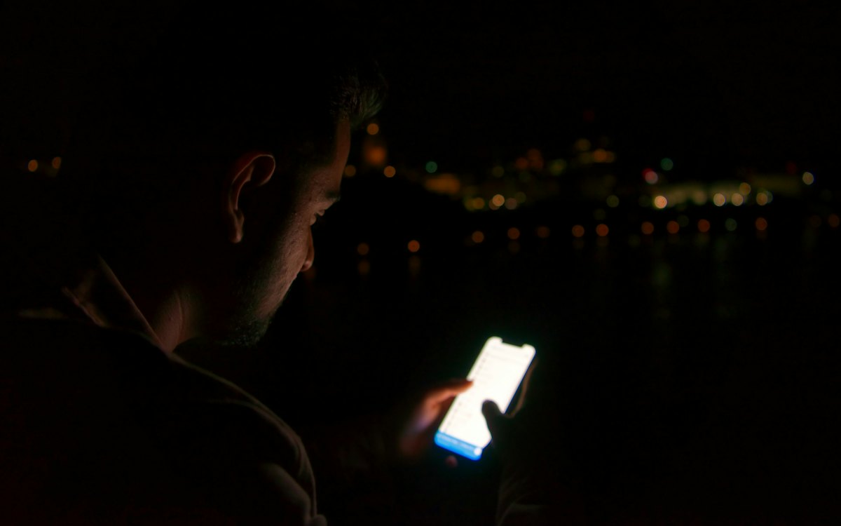 Pessoa olhando o celular no escuro à noite